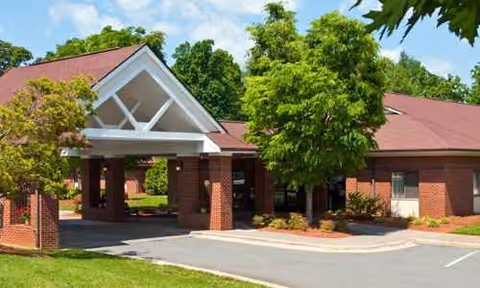 Brick building with a covered entrance and surrounding green trees.