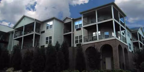Multi-story senior living building with balconies and arched ground-floor entrances.