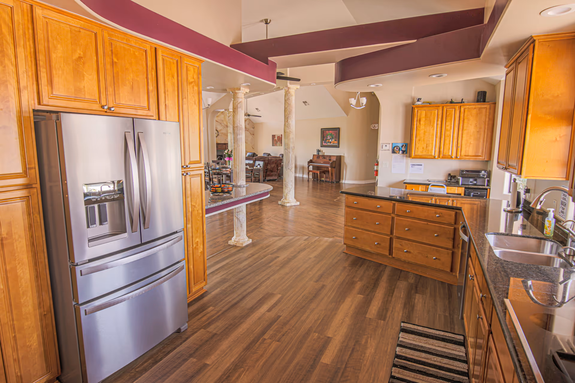 Spacious open-plan kitchen with wooden cabinets, a stainless steel refrigerator, center island and hardwood floors opening to a living area.