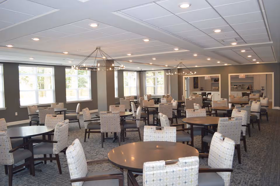 Spacious dining room with multiple round tables and upholstered chairs under ceiling lights.