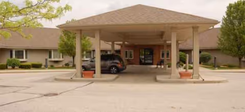 Covered entrance with parked cars at Brookdale Granger and potted plants.