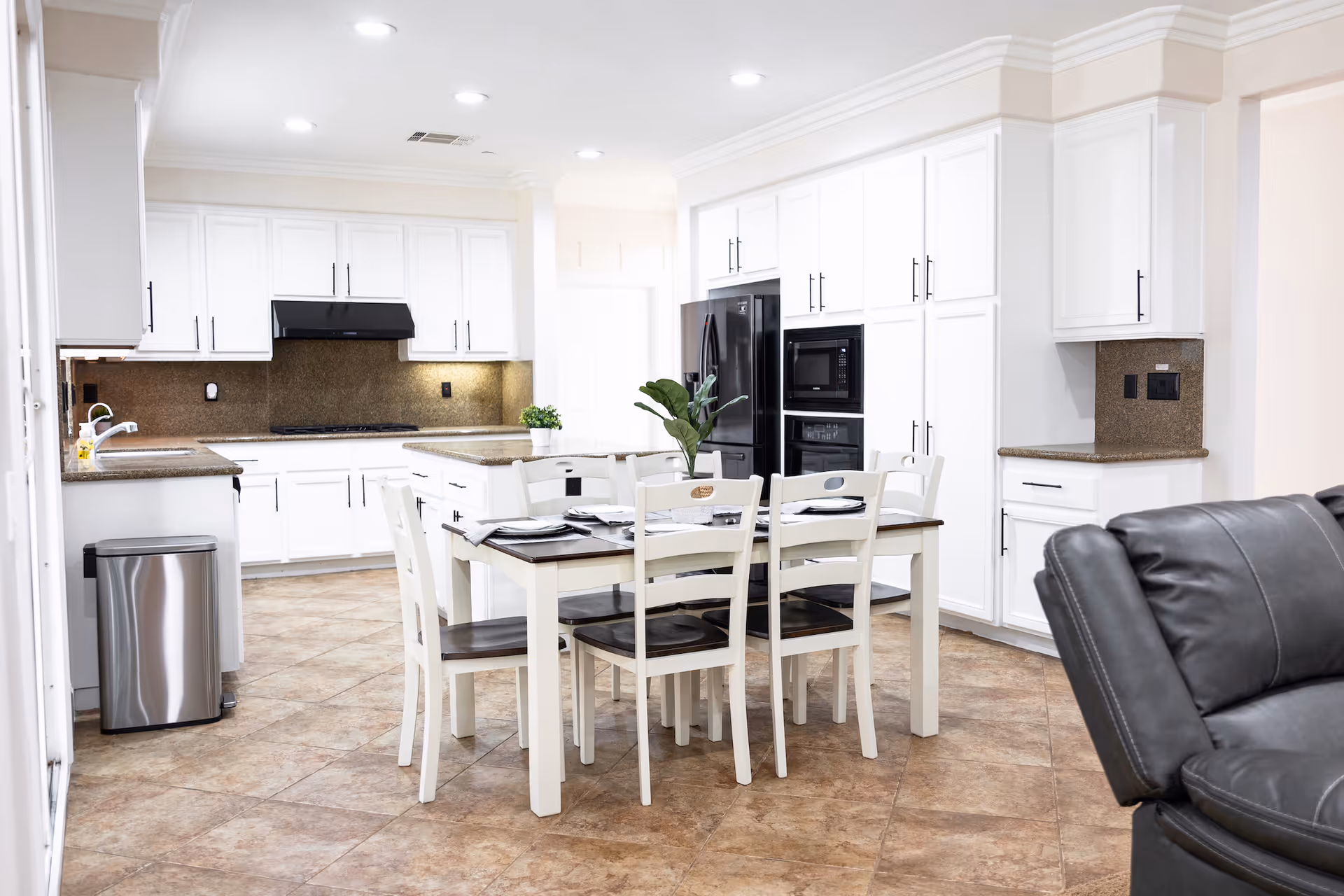 Bright open kitchen with white cabinets, a central dining table and chairs, and stainless appliances.