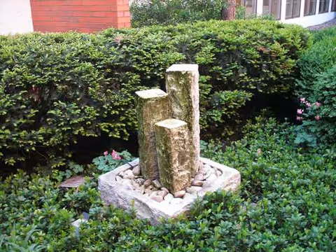 Stone water feature surrounded by hedges and greenery in a landscaped garden.