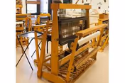 A large wooden weaving loom and additional looms with chairs in a bright craft activity room.