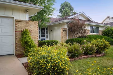 Front exterior of Serenity House IV with shrubs, flowers, and a paved entry.