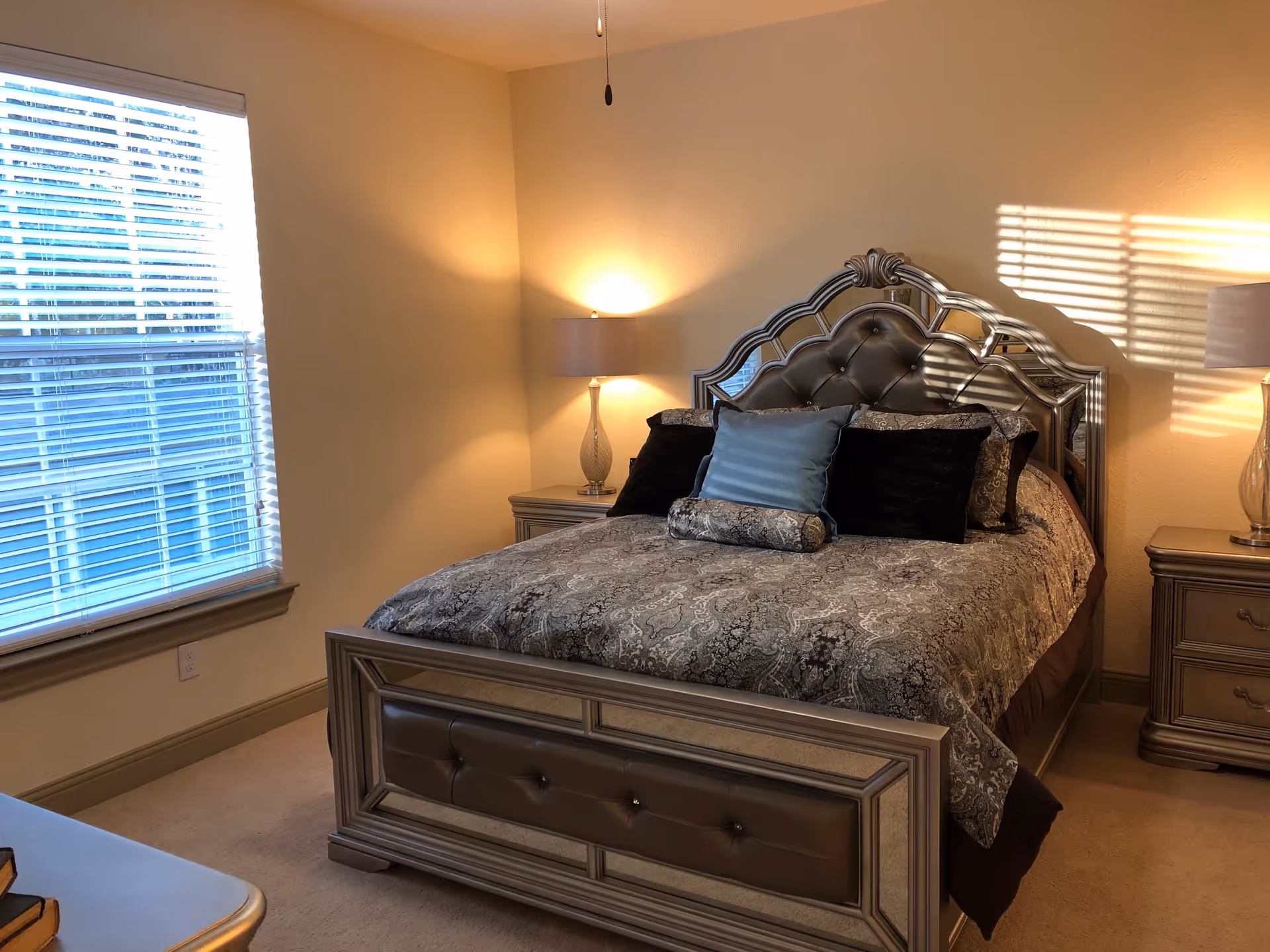 Well-decorated bedroom with an ornate bed, bedside tables and lamps, and a window with blinds.
