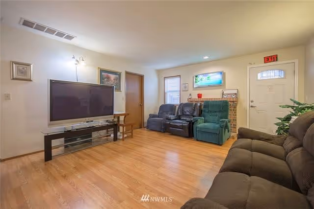 Spacious living room with hardwood floors, multiple recliner sofas, a large flat-screen TV on a stand, and an entry door.