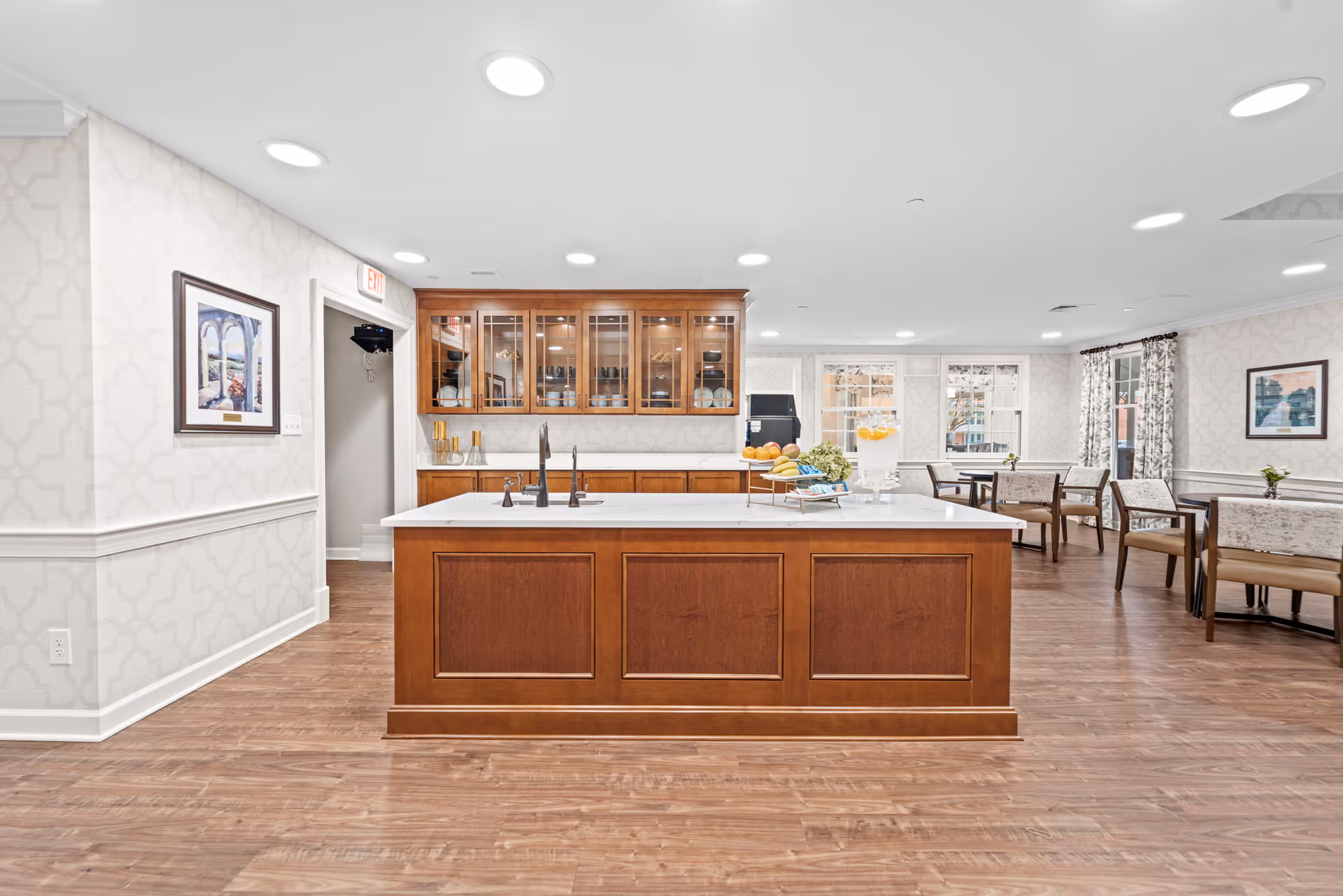 Bright communal kitchen and dining area with a large wooden island, sink, cabinetry, and tables for seating.