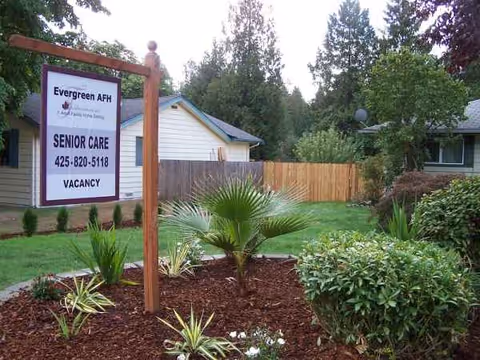 Outdoor view shows Evergreen AFH senior care sign in front yard with landscaped plants.