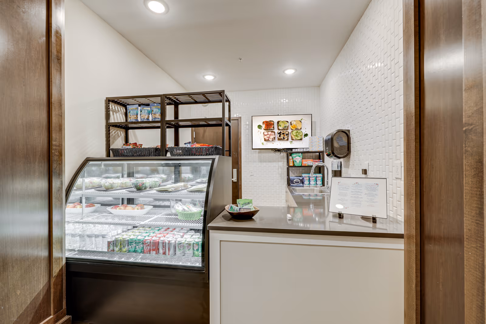 A small café-style service area with a glass refrigerated display case of salads and canned drinks, shelving, and a counter with a menu.