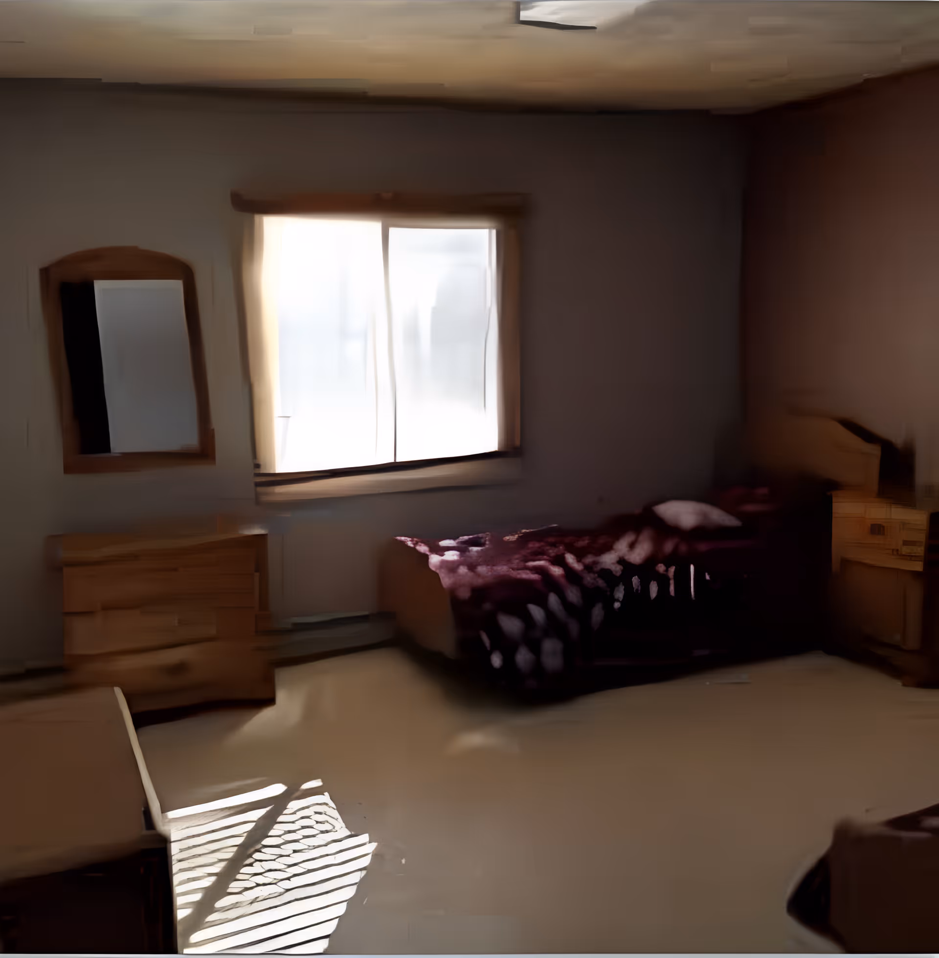 A dimly lit bedroom with a single bed covered in a dark patterned blanket, a wooden dresser with a mirror on the left wall, and a window with curtains letting in some light. There is also a chair casting shadows on the floor.