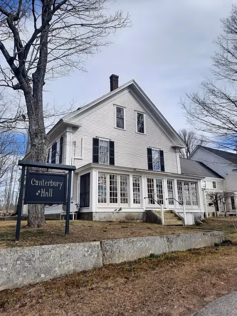 White two-story senior living facility with Canterbury Hall sign and enclosed porch.