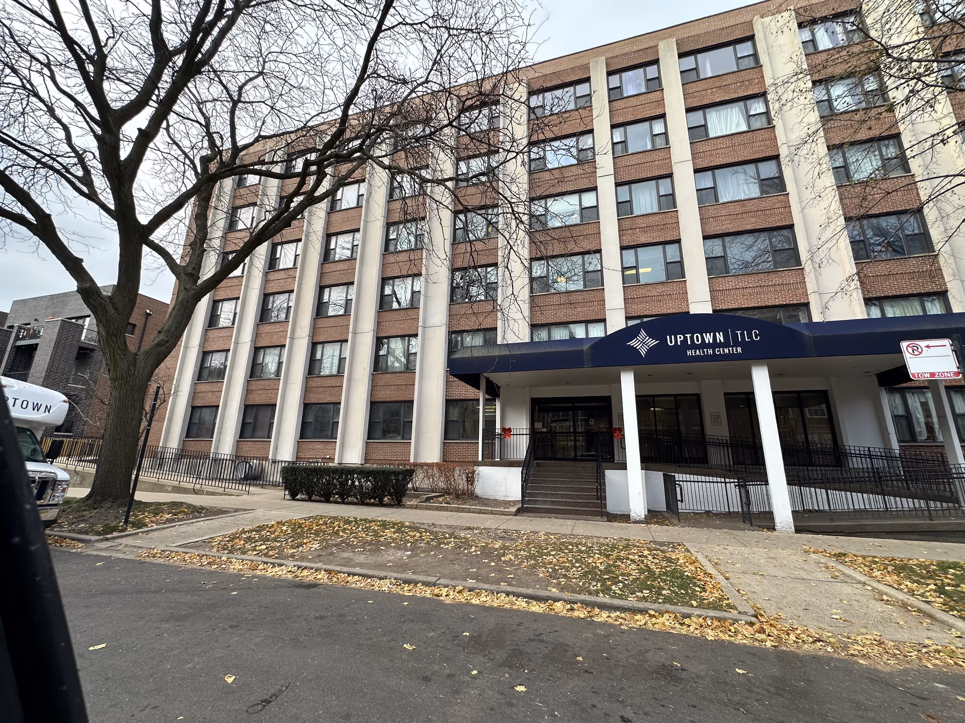 Front exterior of the multi-story Uptown TLC Health Center building with a covered entrance and sidewalk.