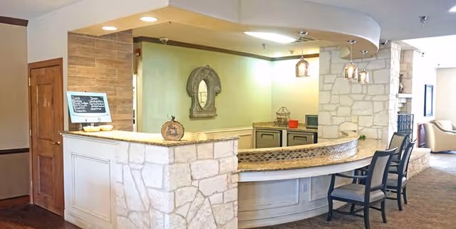 Curved stone-faced counter with bar chairs, pendant lights, and seating in a bright interior common area.