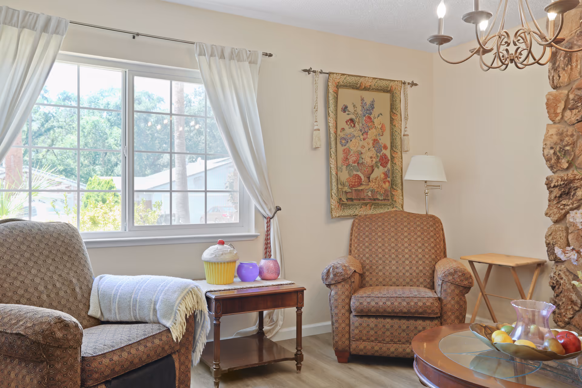 Cozy living room with two upholstered armchairs, a window with white curtains, side tables and decorative accents.