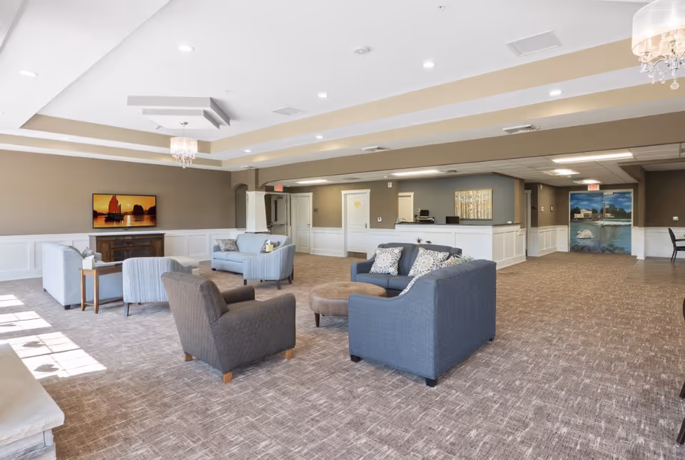 Spacious furnished common lounge with sofas, armchairs, a wall-mounted TV and a reception desk in the background.