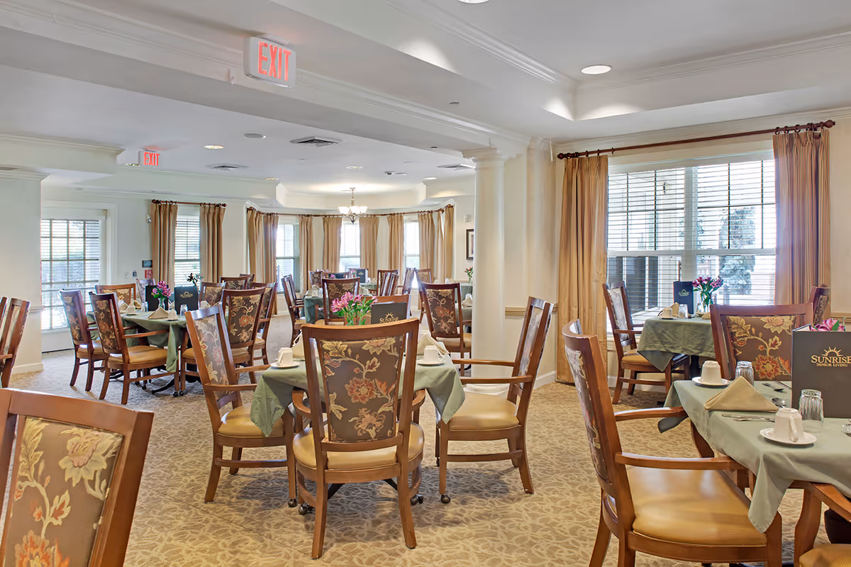 Spacious, well-lit dining room with multiple tables set for meals and floral-upholstered chairs.