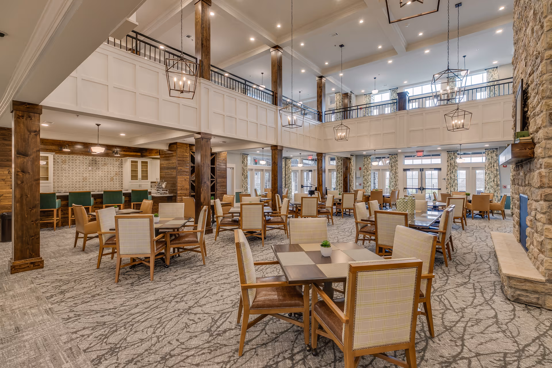 Spacious two-story dining and lounge area with multiple tables and chairs, high ceilings, a balcony, and a stone fireplace.