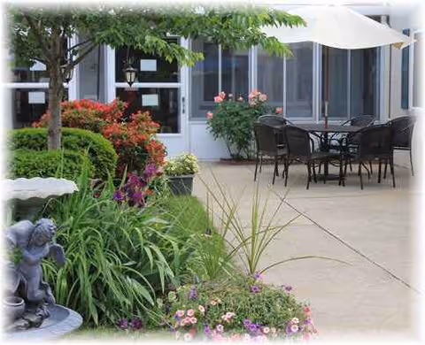 Outdoor patio seating with tables, chairs, umbrellas, and garden near the facility entrance.