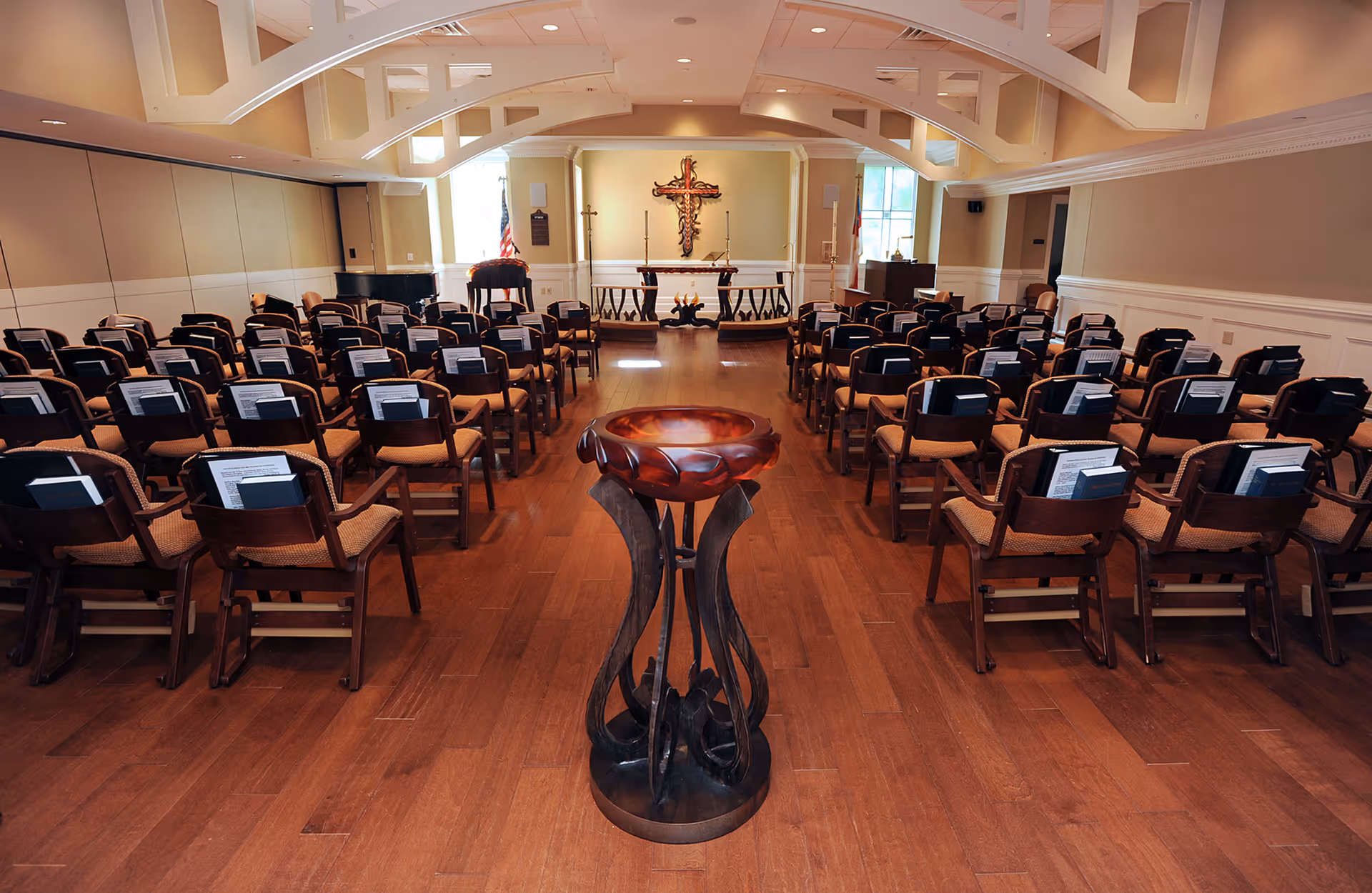 A chapel-like interior with rows of chairs facing an altar and large cross, with a carved wooden lectern in the foreground.
