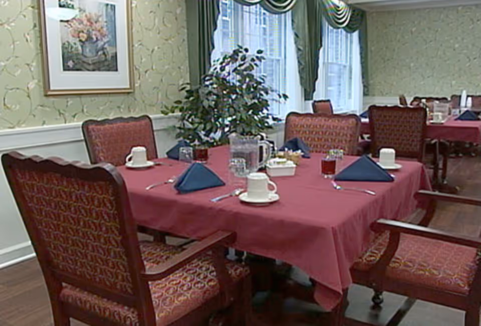 Dining room with a table set with a red tablecloth, napkins, cups and upholstered chairs.