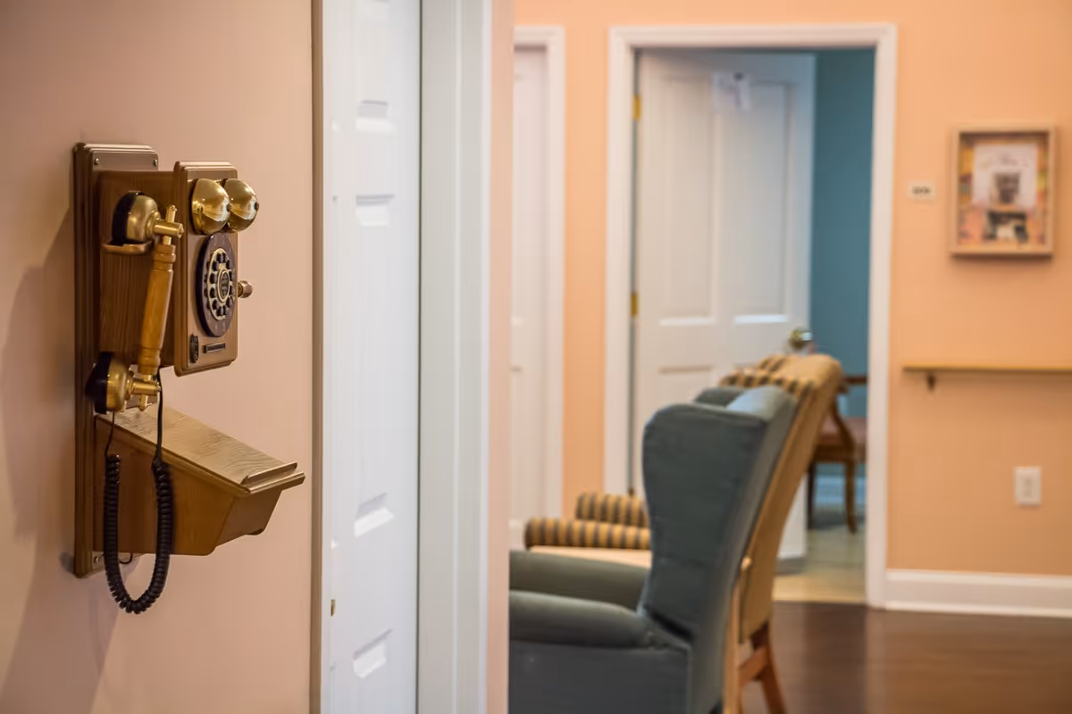 Wall-mounted vintage telephone on a peach-colored hallway wall with armchairs visible in a sitting area beyond.
