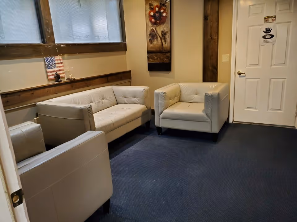 Small waiting lounge with gray leather chairs, a sofa, wall art, and door.