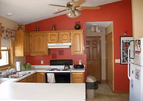 Kitchen area of Doherty Home with wooden cabinets, red walls, stove, sink, and ceiling fan.