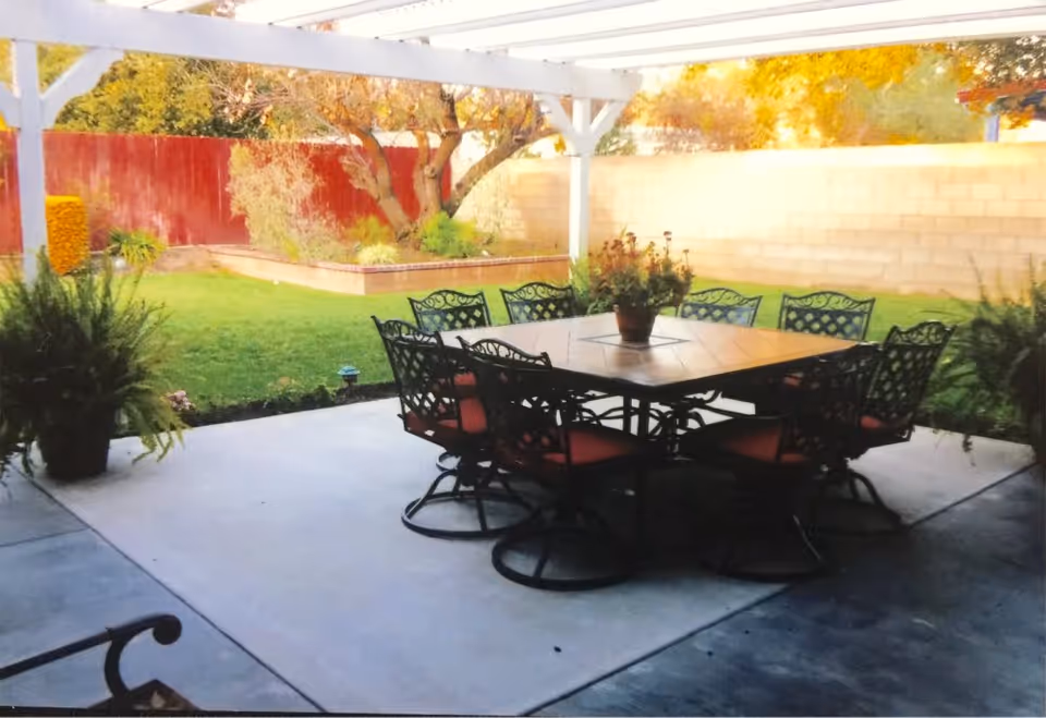 Covered backyard patio with a large outdoor dining table and chairs overlooking a lawn and garden.