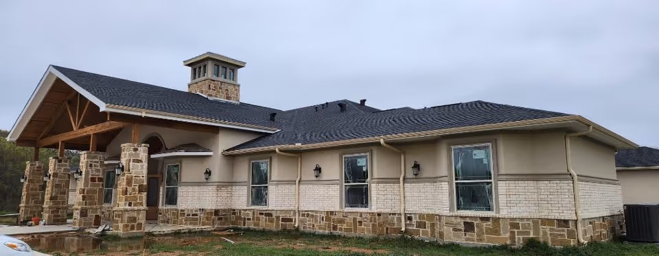Single-story memory care building with stone and brick exterior, covered wooden entrance, and multiple windows under an overcast sky.
