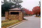 Entrance sign for Bob Hope Village made of brick with gold lettering, situated next to a road lined with trees showing autumn foliage.