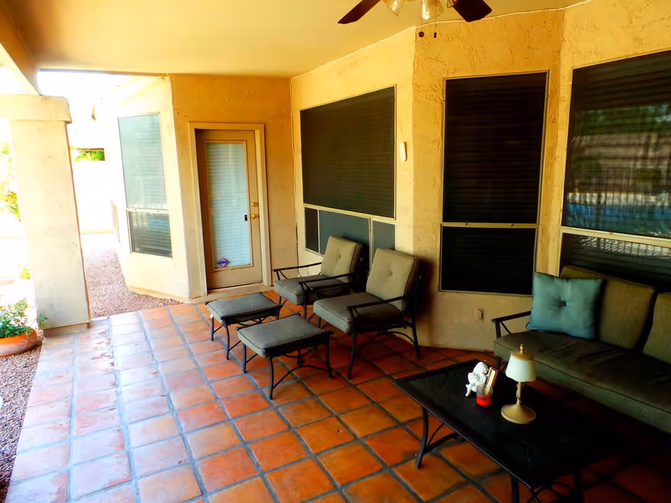 Covered outdoor patio with terracotta tile floor, cushioned lounge chairs, a sofa and a coffee table.