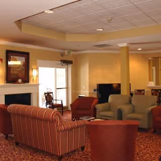 Cozy communal lounge with upholstered sofas and armchairs arranged around a fireplace and television.