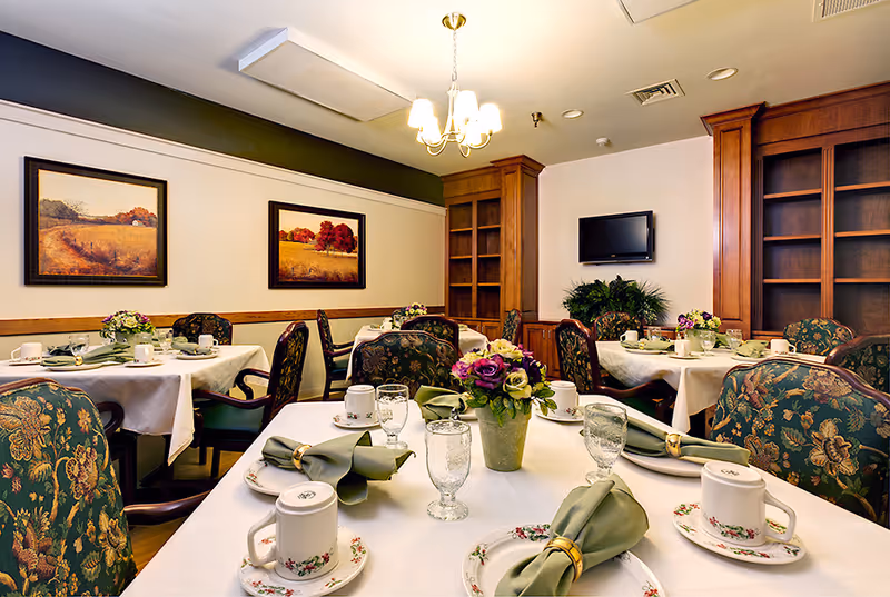 A formal dining room with tables set with floral china, green napkins, and floral centerpieces.