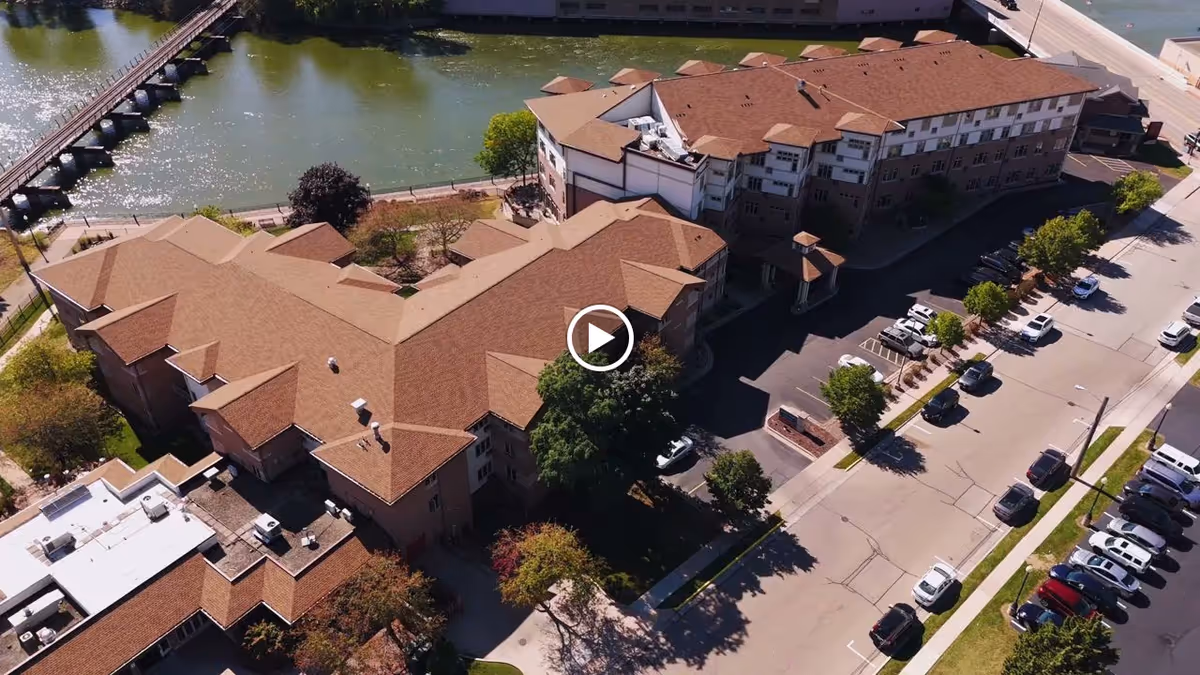 Aerial view of a multi-wing senior living building beside a river with surrounding parking and walkways.