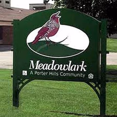 Meadowlark Retirement Village sign on a green lawn with a cardinal graphic.