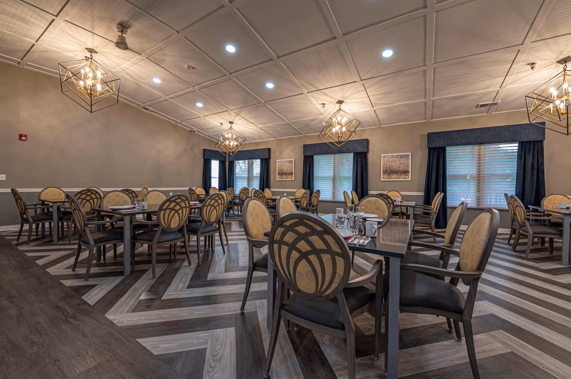 Elegant dining room with multiple tables and upholstered chairs, geometric pendant lights, and a chevron-patterned floor.