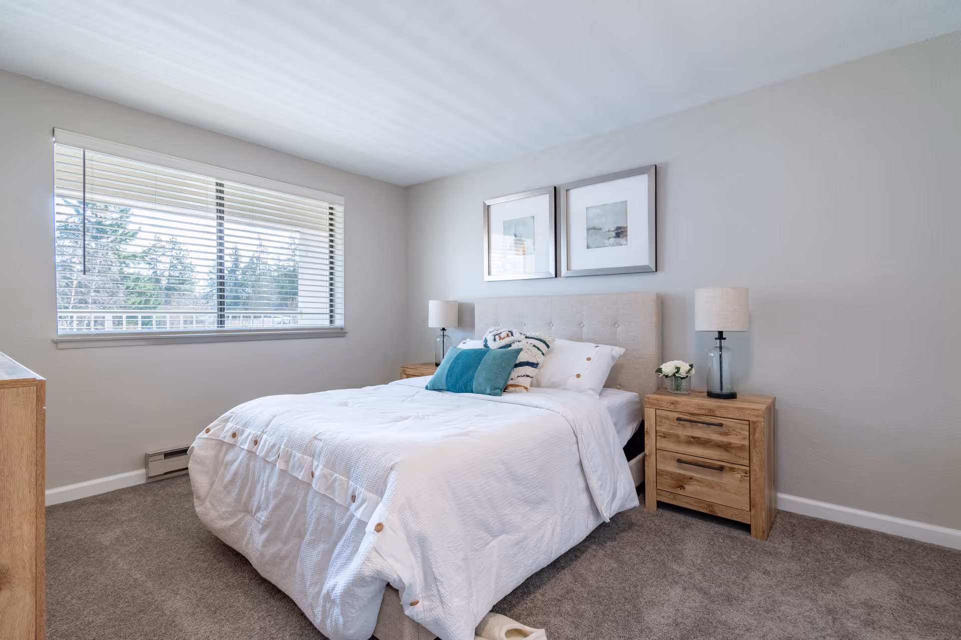 A tidy bedroom featuring a bed with white bedding, wooden nightstands and lamps, framed artwork above the headboard, and a large window.