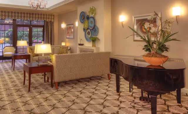 A comfortable lounge with sofas, side tables and lamps, decorative wall art, and a grand piano topped with a plant.