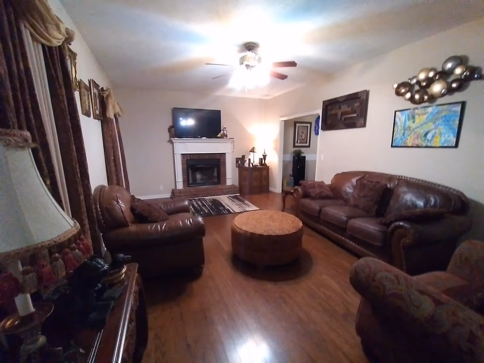 Cozy living room with leather sofas, a round ottoman, hardwood floors, a fireplace with a TV above, and wall art.