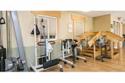 Indoor rehabilitation gym featuring exercise machines and a wooden staircase nearby.