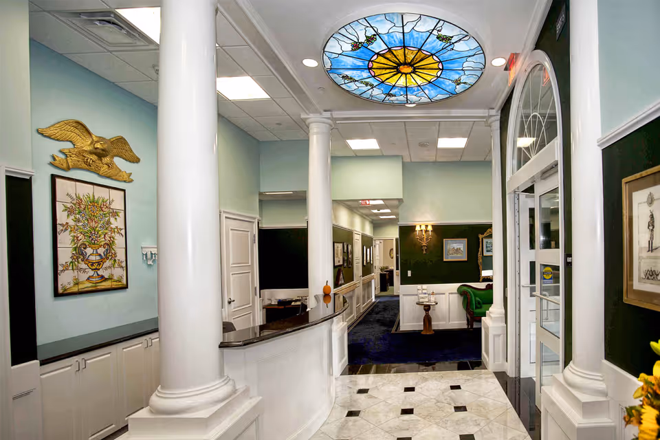 Bright, elegant reception lobby with white columns, marble tile floor, a stained-glass ceiling medallion, and a seating area down the hall.