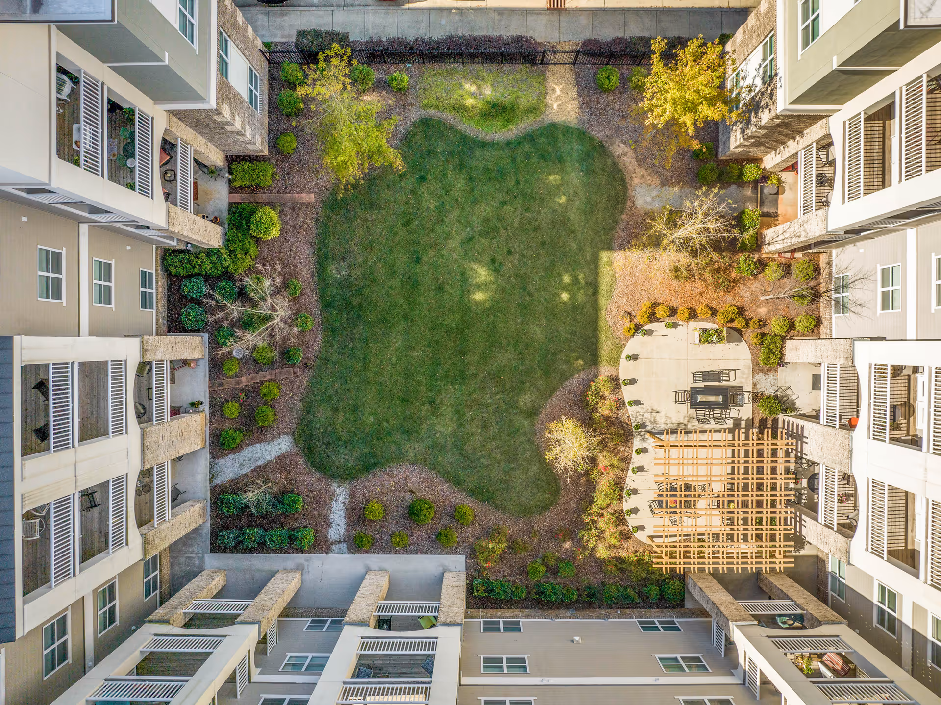 Aerial view of a landscaped central courtyard with a grassy lawn, walkways, patio seating and surrounding apartment balconies.