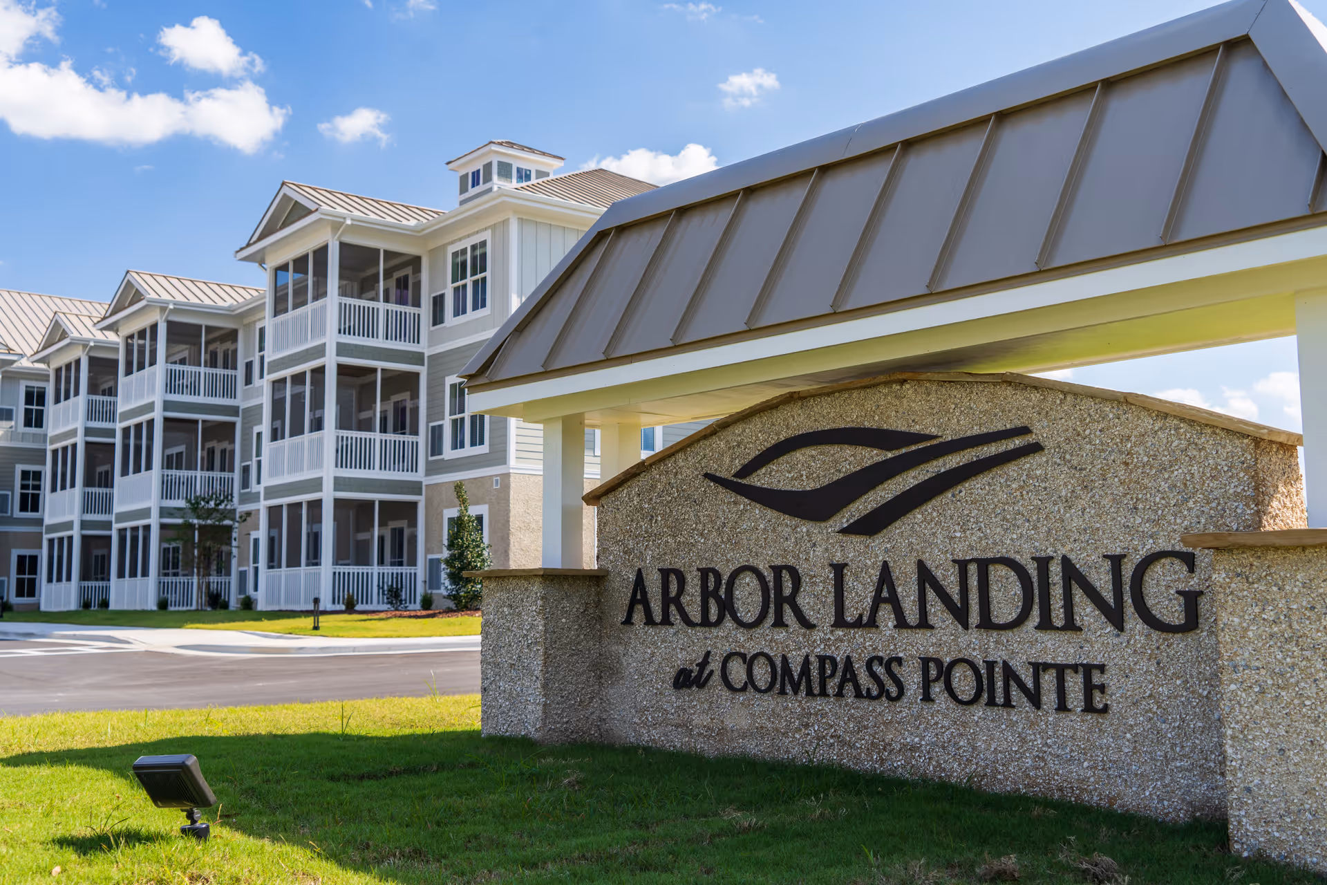 Entrance stone sign reading "Arbor Landing at Compass Pointe" with the facility's multi-story apartment building and screened balconies in the background.