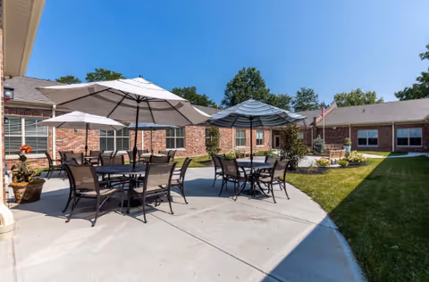 Outdoor courtyard with several patio tables, umbrellas and chairs on a concrete patio beside a brick building.