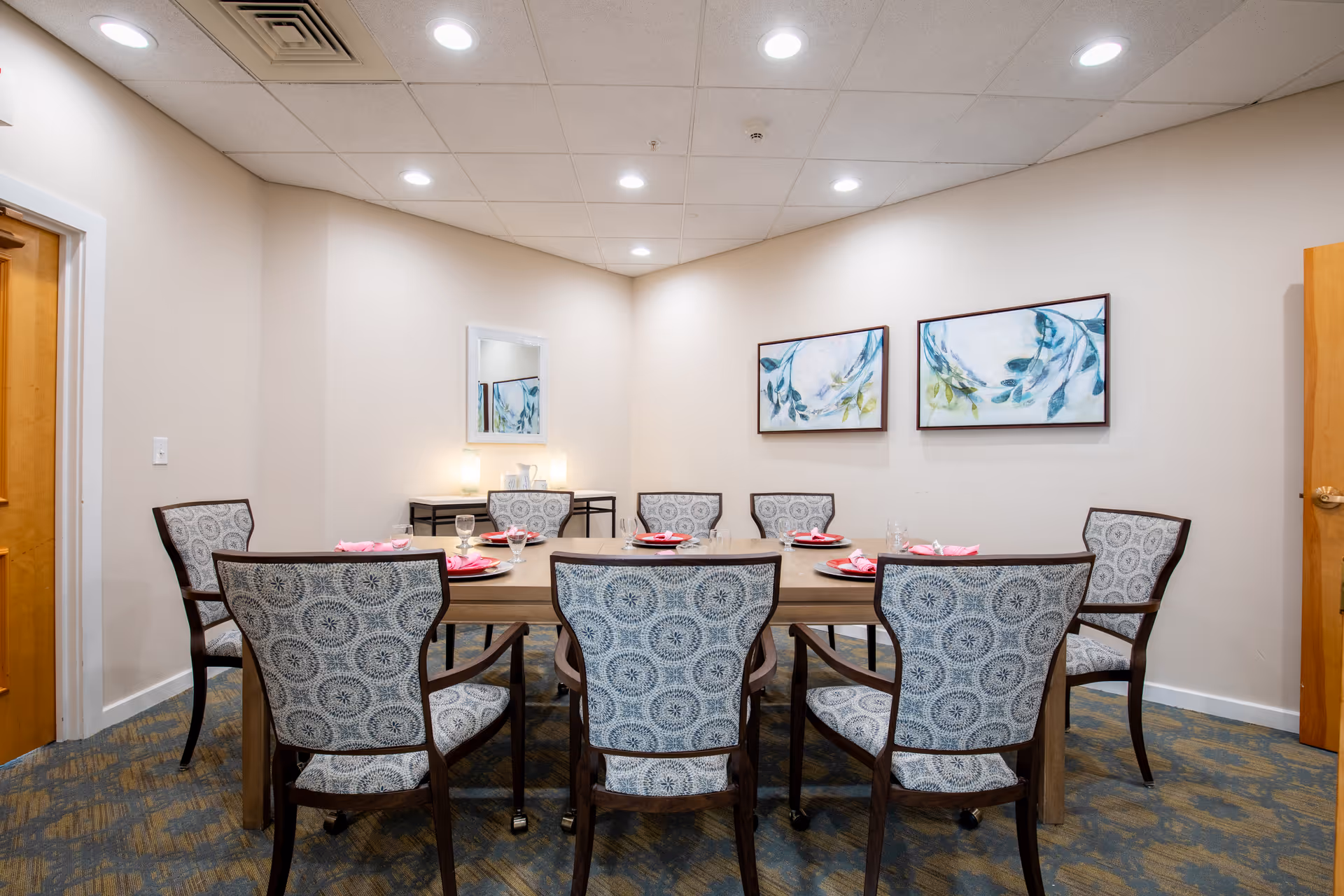Private dining room with a round wooden table set for six and patterned upholstered chairs, wall art, and a console table with a mirror.