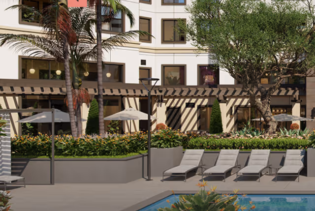 Poolside courtyard with lounge chairs, umbrellas, palm trees, landscaping, and a multi-story building facade.