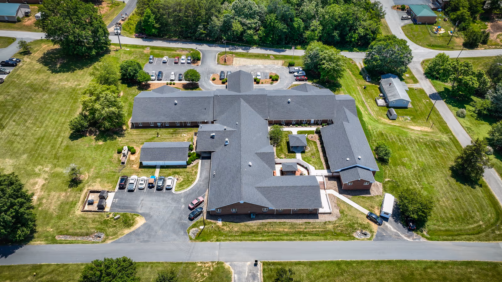Aerial view of Walnut Ridge Assisted Living facility showing a large, single-story building with a dark roof surrounded by green lawns, trees, parking lots with several cars, and nearby roads.