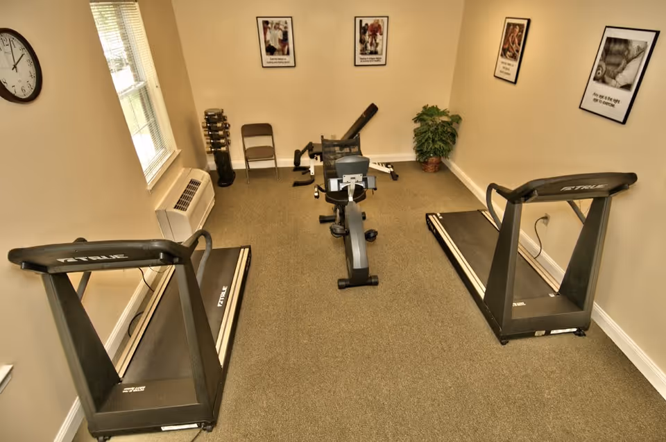 Small exercise room with two treadmills, a recumbent bike, free weights, and framed posters on the walls.