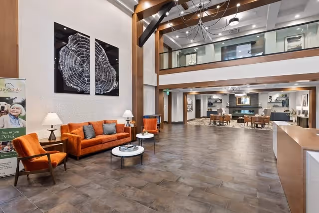 Spacious two-story lobby of a senior living facility with orange sofas, tables, and a reception desk.
